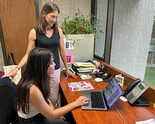 Instructor standing and student on laptop computer in office