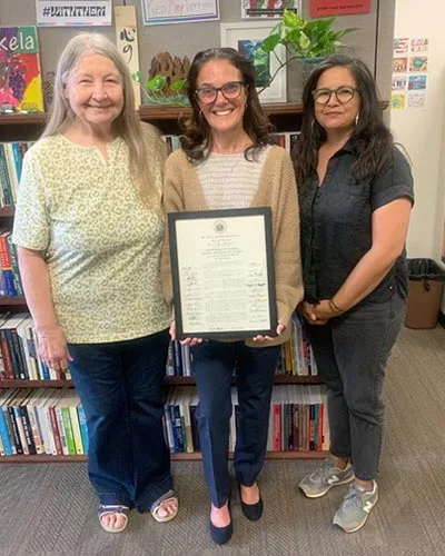 Three smiling women holding a proclamation.