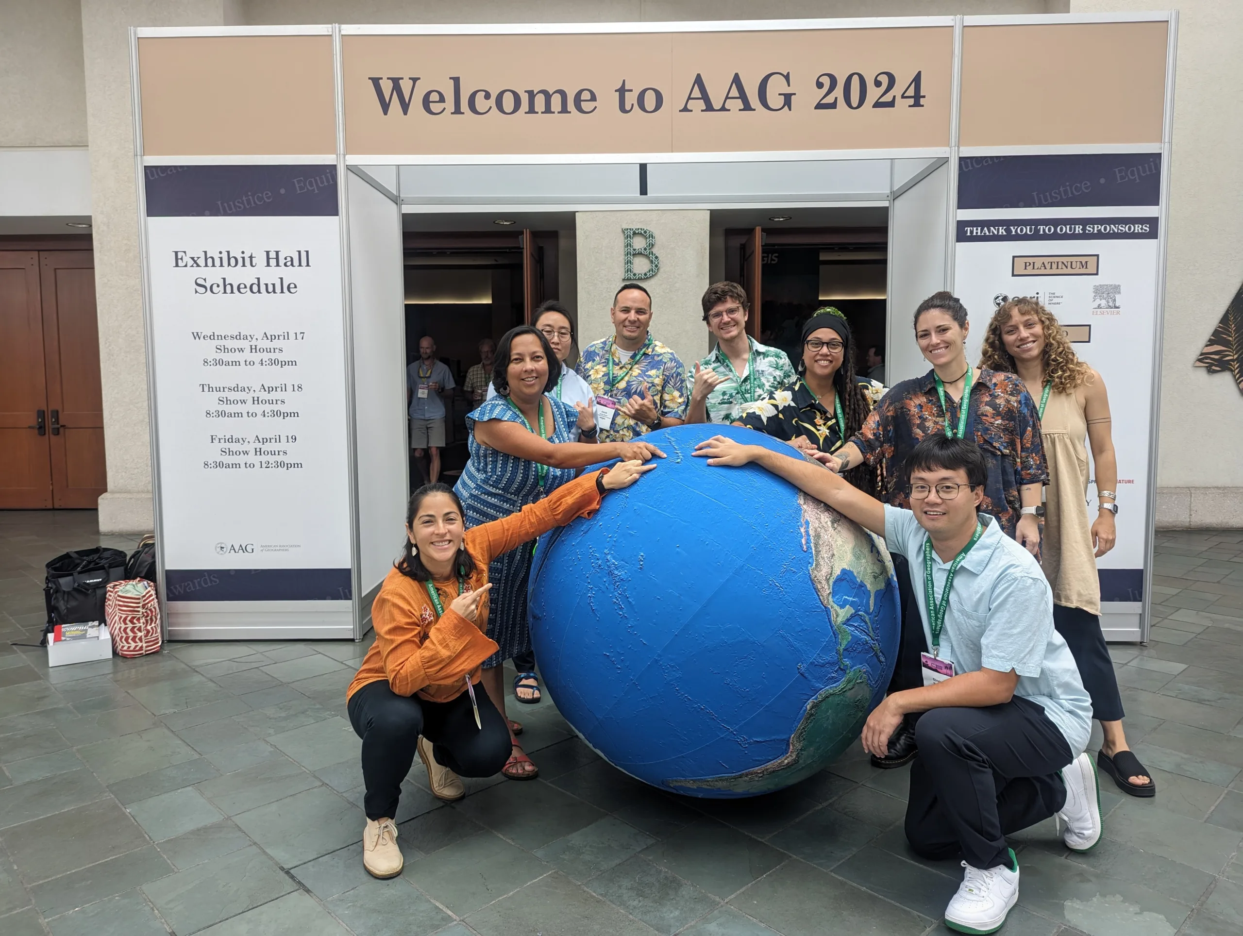 Group of people with giant globe pointing at Hawaiʻi located in the middle of the Pacific Ocean.